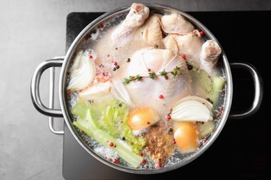 Photo of Whole fresh turkey, cut onion, celery and spices boiling in pot on stove on grey table, top view