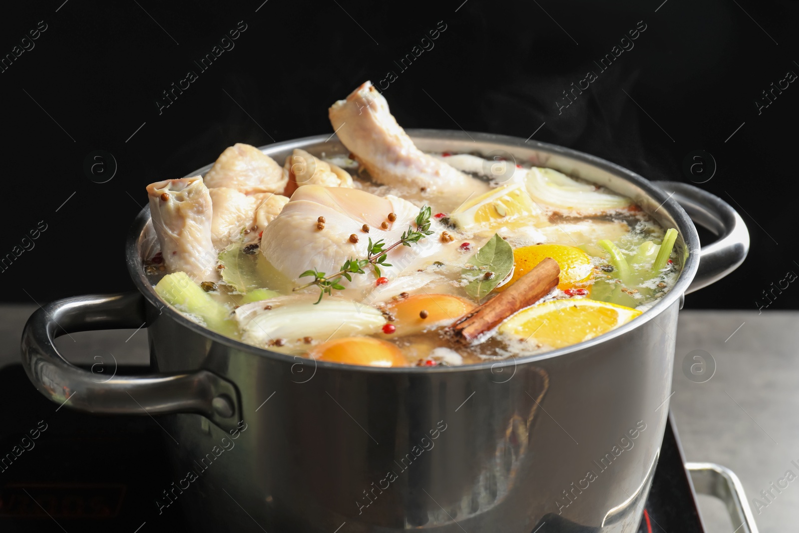 Photo of Whole fresh turkey, cut citrus fruits, thyme and spices boiling in pot on stove against black background, closeup