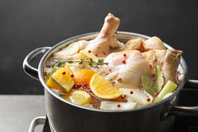 Photo of Whole fresh turkey, cut citrus fruits and spices boiling in pot on table against black background, closeup