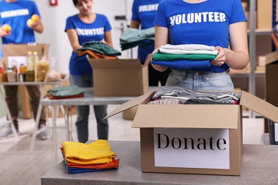 Photo of Group of volunteers packing donation goods at tables indoors, selective focus