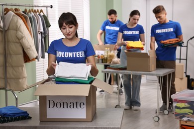 Photo of Group of volunteers packing donation goods at tables indoors, selective focus