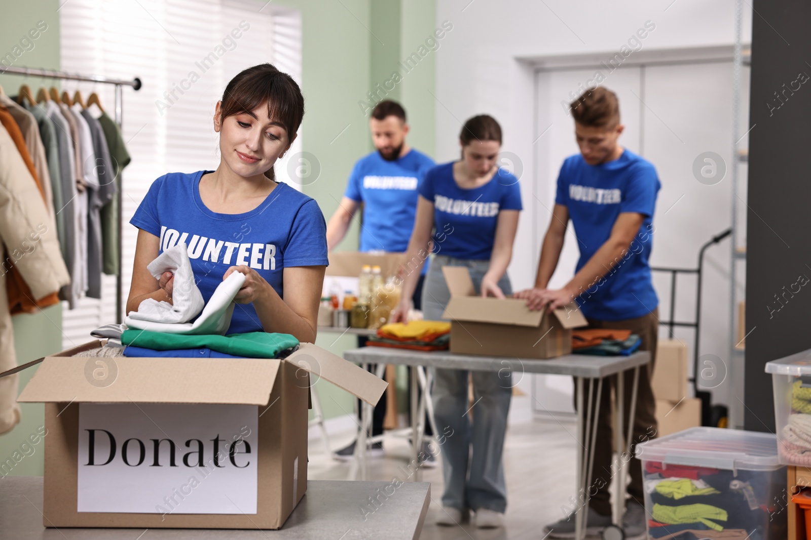 Photo of Group of volunteers packing donation goods at tables indoors, selective focus