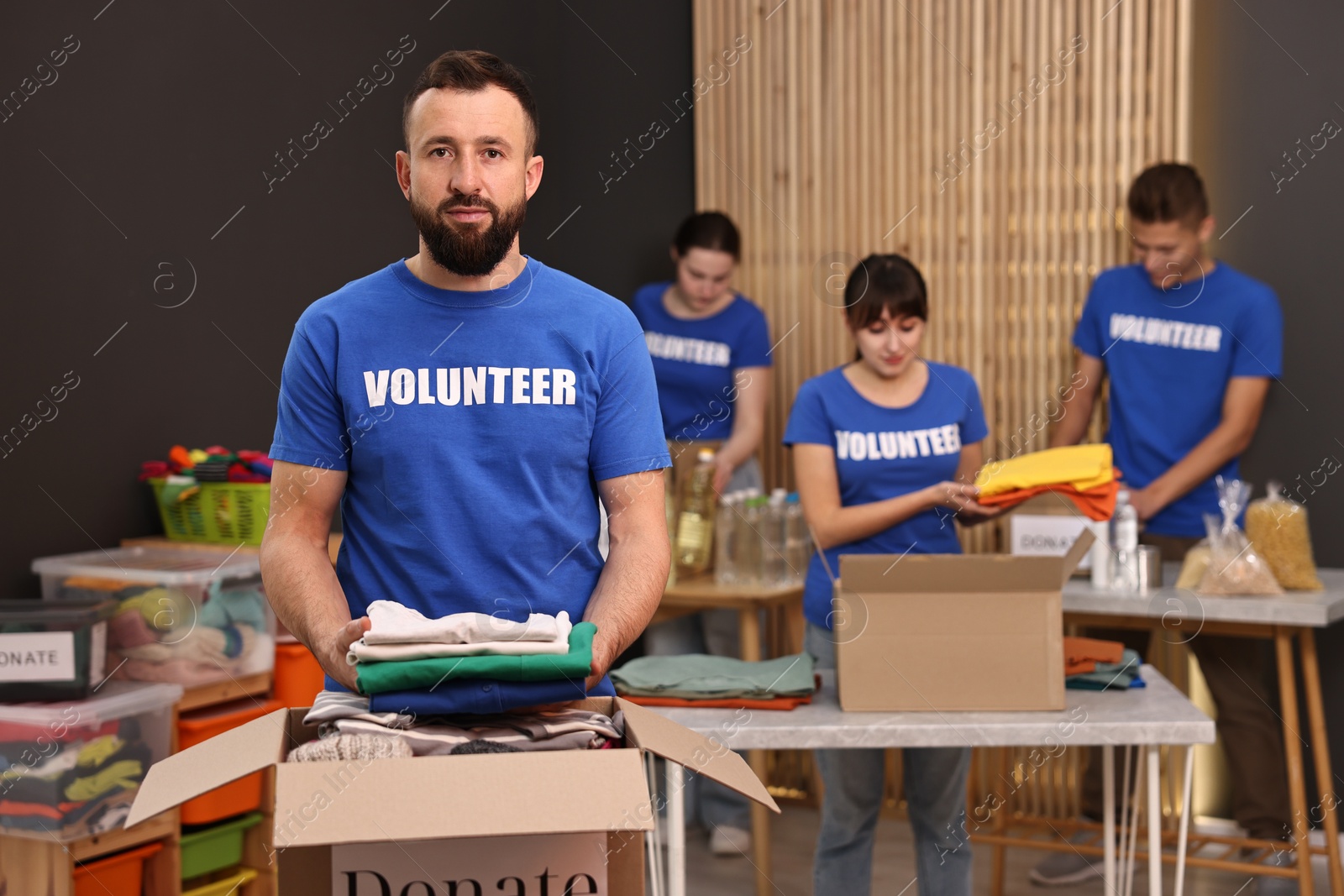 Photo of Group of volunteers packing donation goods at tables indoors, selective focus