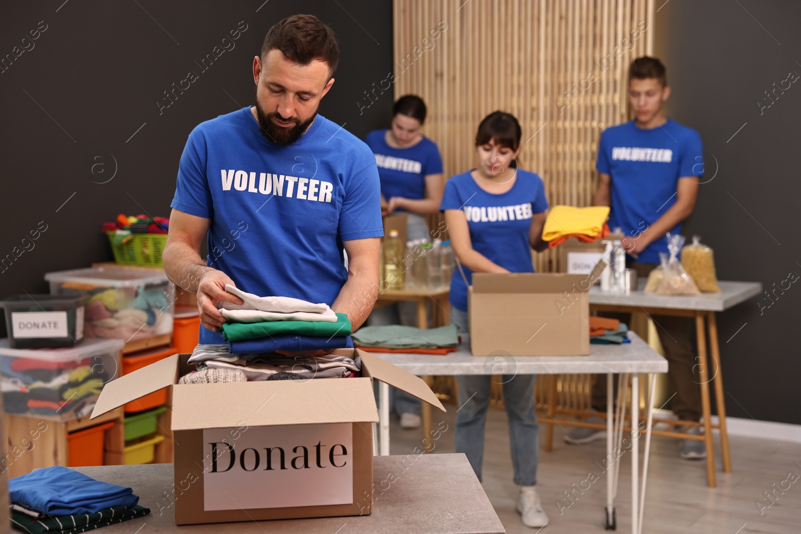 Photo of Group of volunteers packing donation goods at tables indoors, selective focus