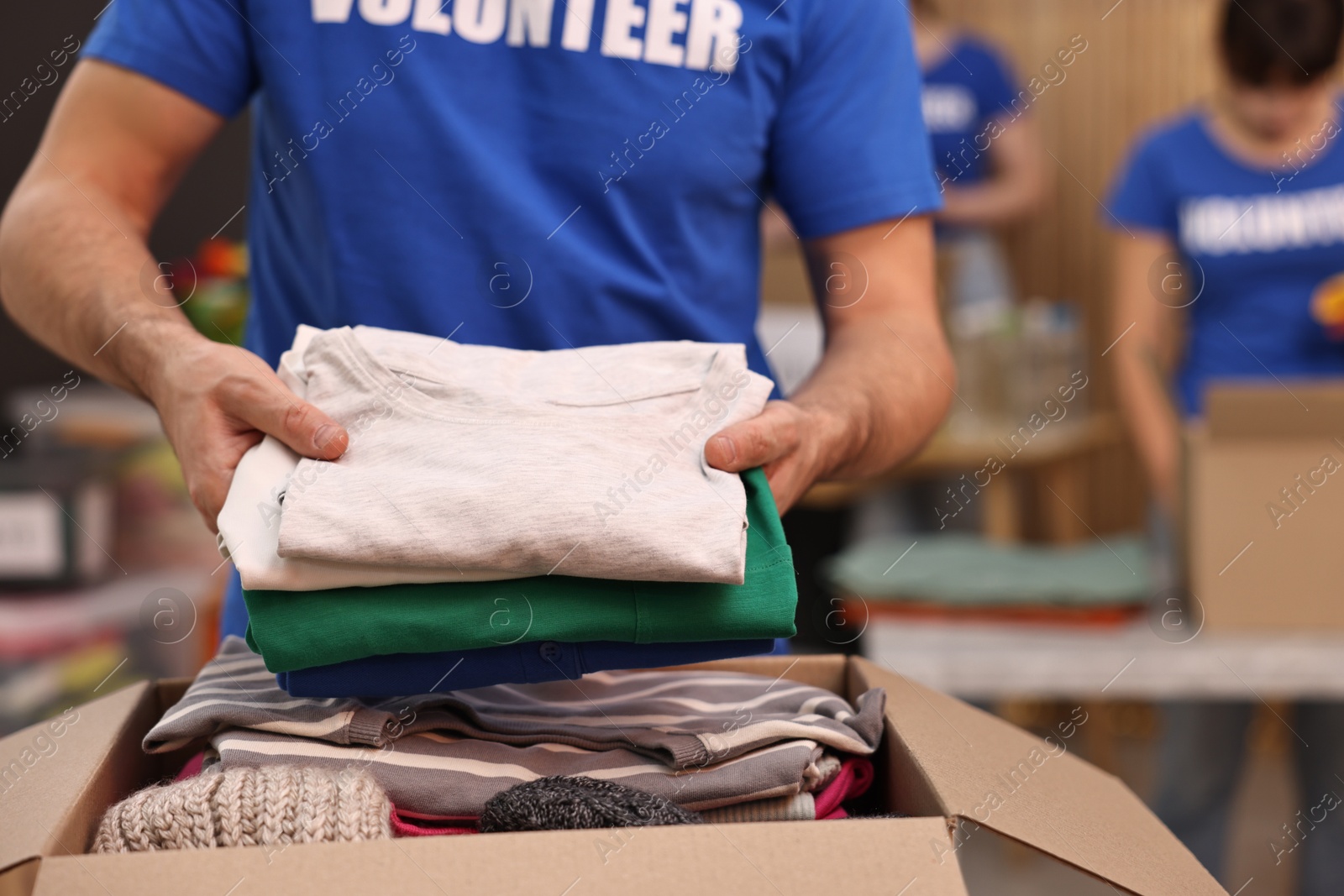 Photo of Volunteer putting clothes into donation box indoors, closeup