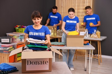 Photo of Group of volunteers packing donation goods at tables indoors, selective focus