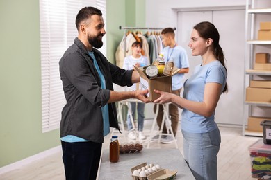 Photo of Volunteers holding donation box with food products indoors, selective focus