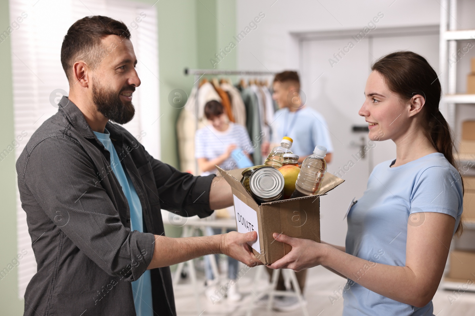 Photo of Volunteers holding donation box with food products indoors, selective focus