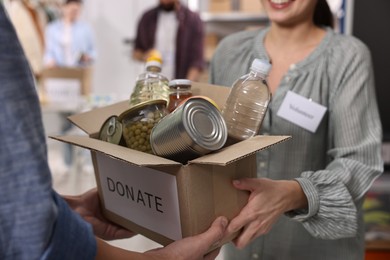 Photo of Volunteers holding donation box with food products indoors, closeup