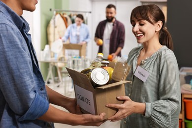 Photo of Volunteers holding donation box with food products indoors, selective focus