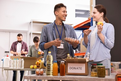 Photo of Volunteers packing food donations at tables indoors, selective focus