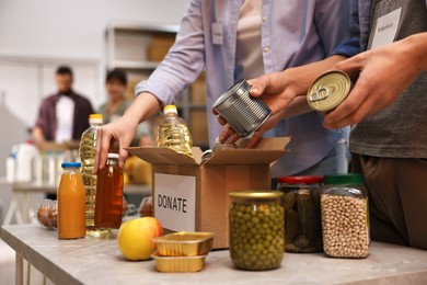 Photo of Volunteers packing food donations at table indoors, closeup