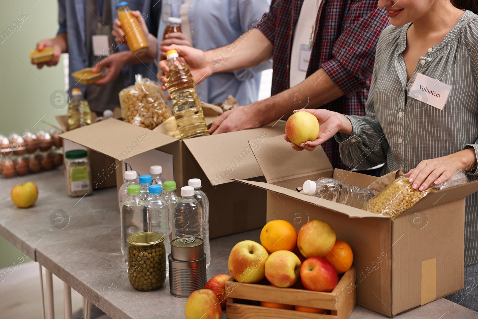 Photo of Group of volunteers packing food donations at table indoors, closeup