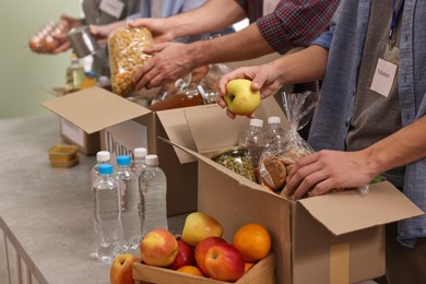 Photo of Group of volunteers packing food donations at table indoors, closeup