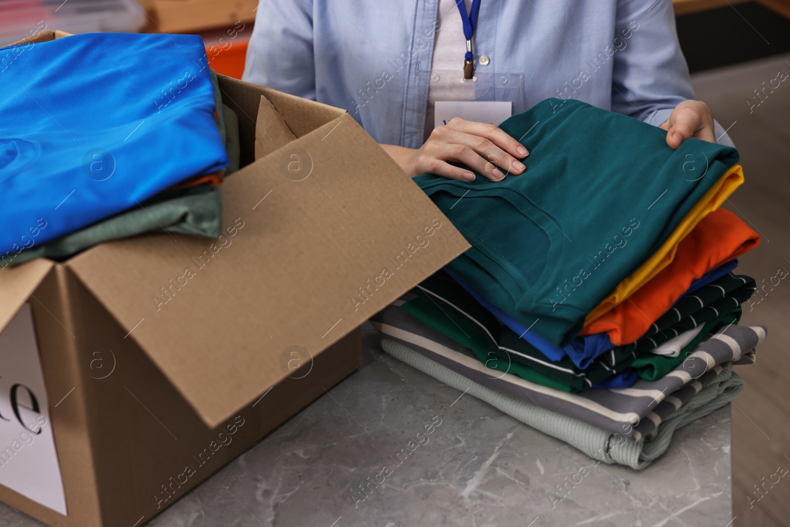 Photo of Volunteer sorting clothes for donation at table indoors, closeup