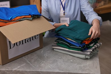 Photo of Volunteer sorting clothes for donation at table indoors, closeup