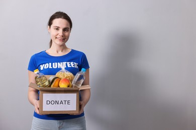 Photo of Woman holding donation box with food products on grey background, space for text