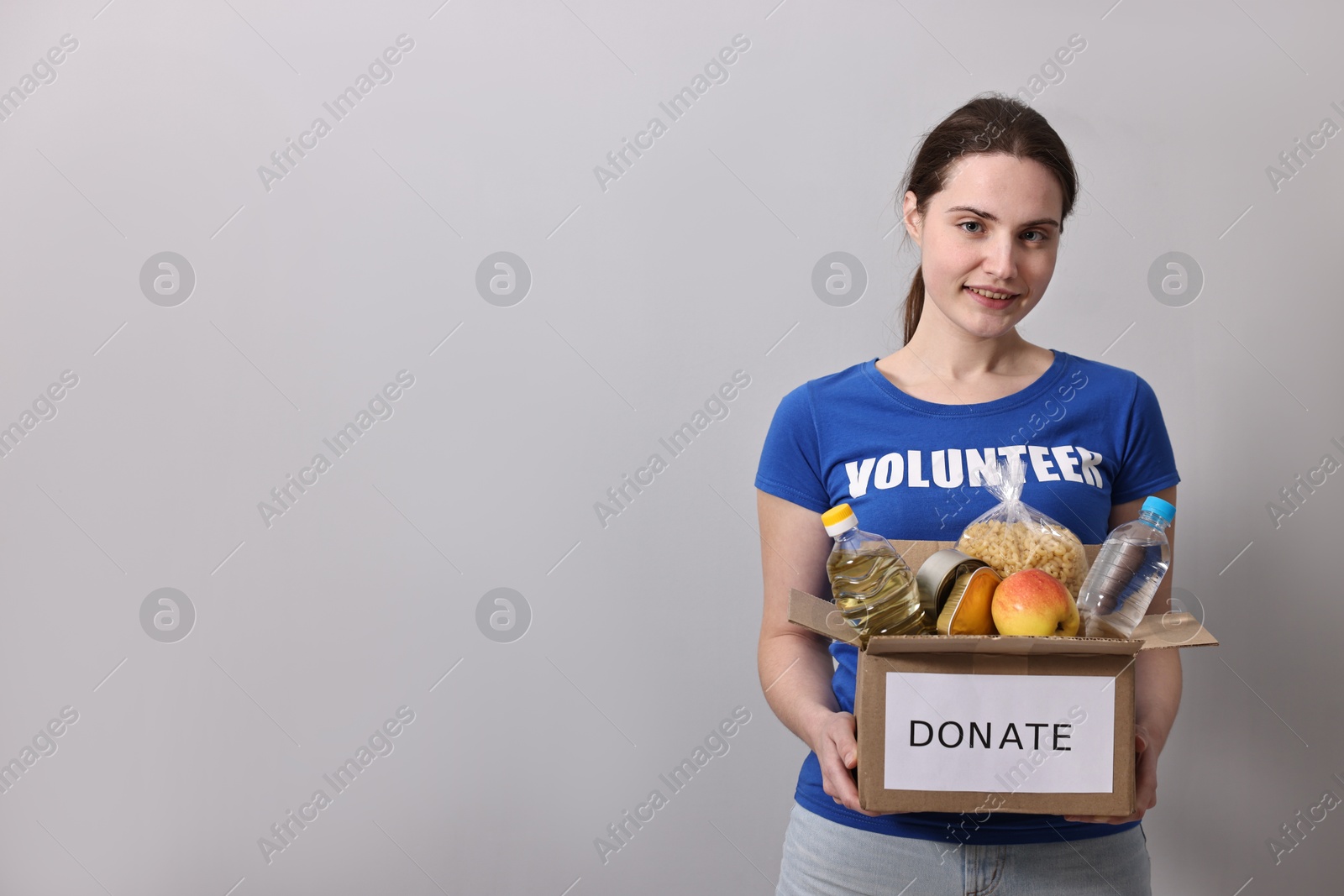 Photo of Woman holding donation box with food products on grey background, space for text