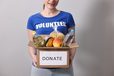 Photo of Woman holding donation box with food products on grey background, closeup