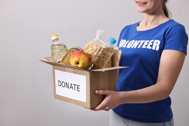 Photo of Woman holding donation box with food products on grey background, closeup. Space for text