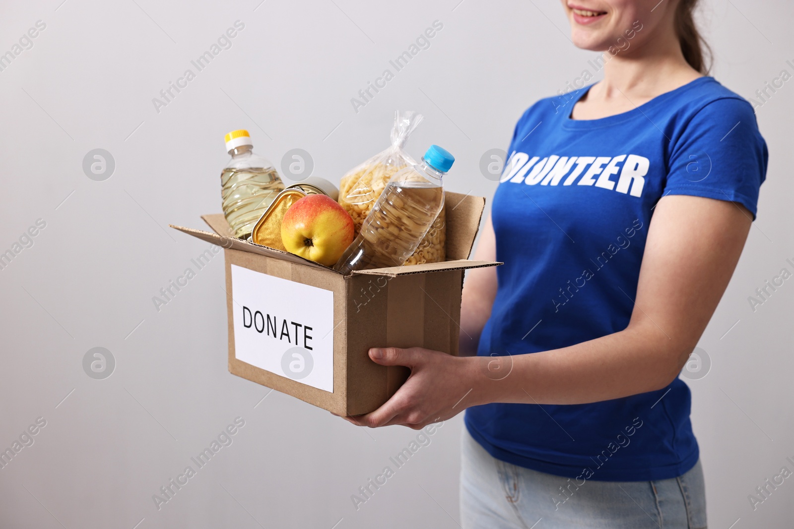 Photo of Woman holding donation box with food products on grey background, closeup. Space for text