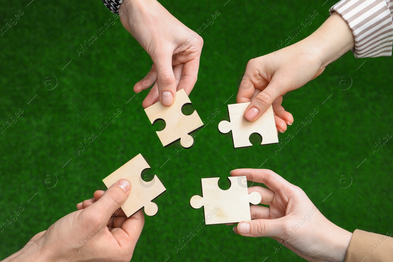 Photo of Teamwork. Group of people putting puzzle pieces together on blurred background, top view