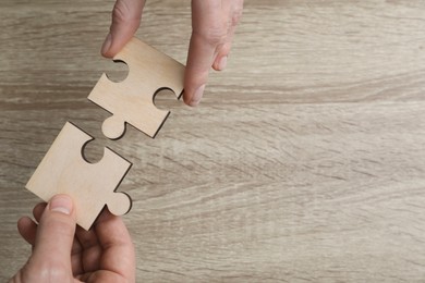 Photo of Teamwork. People putting puzzle pieces together at wooden table, top view. Space for text