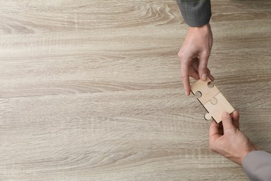 Photo of Teamwork. People putting puzzle pieces together at wooden table, top view. Space for text