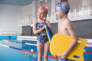 Photo of Children with goggles and kickboards near swimming pool indoors