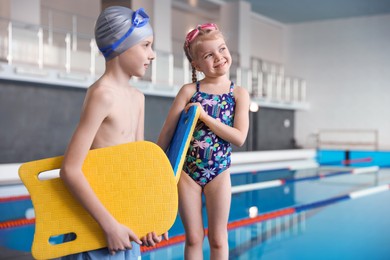 Photo of Children with goggles and kickboards near swimming pool indoors