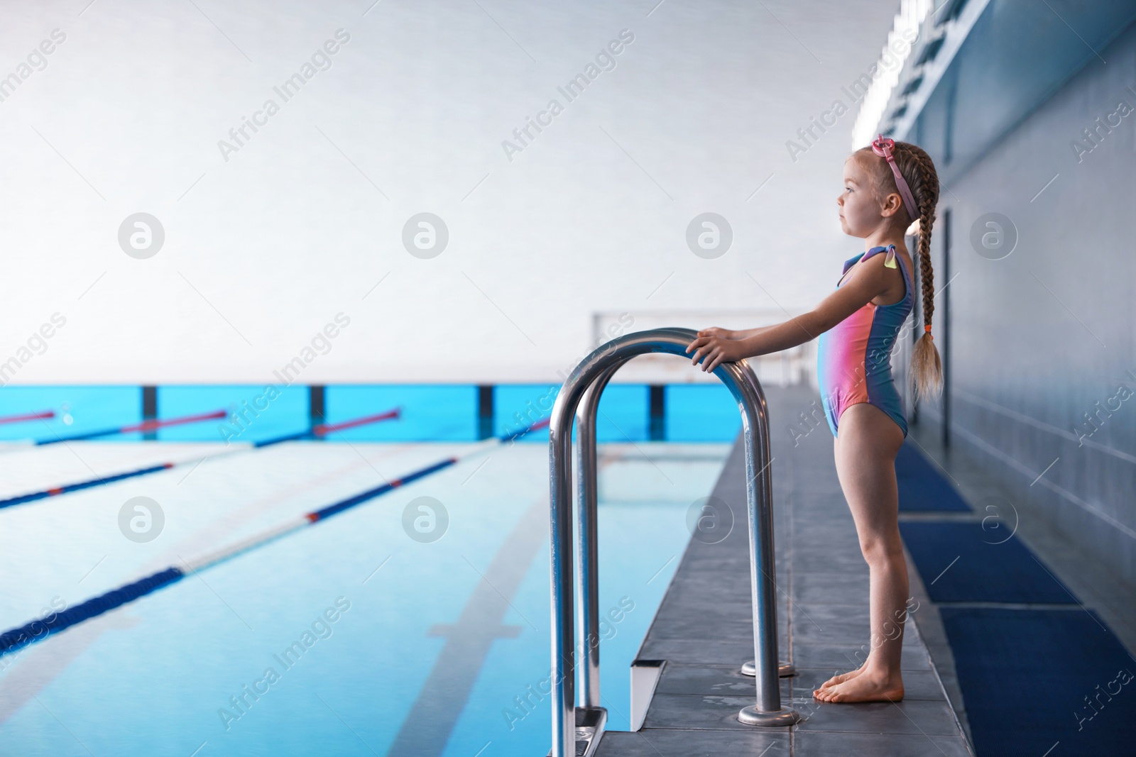 Photo of Little girl wearing swimsuit near swimming pool indoors, space for text