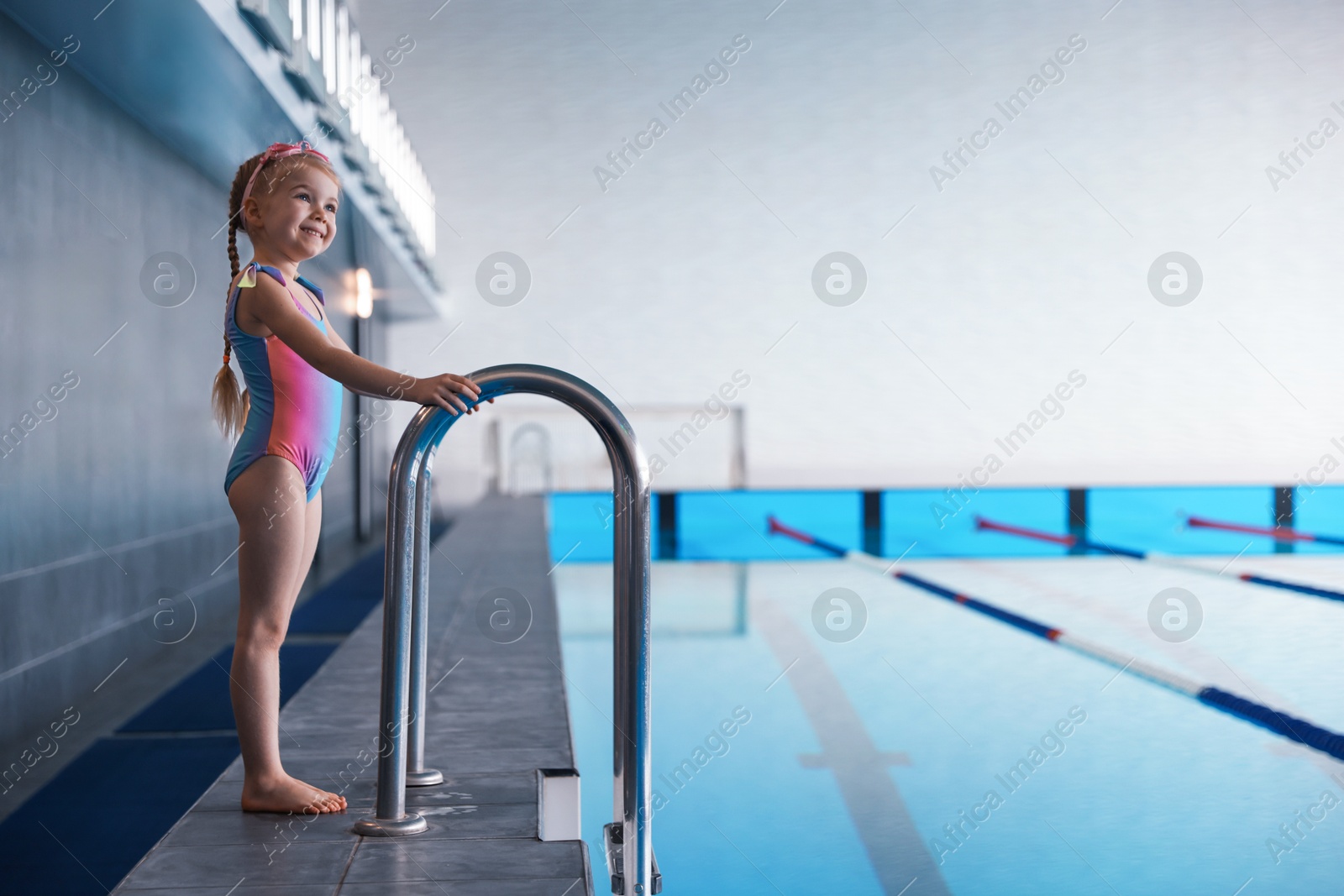 Photo of Little girl wearing swimsuit near swimming pool indoors, space for text