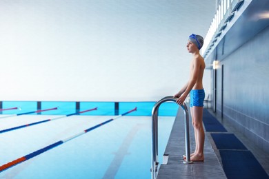 Photo of Boy wearing swimwear near swimming pool indoors, space for text