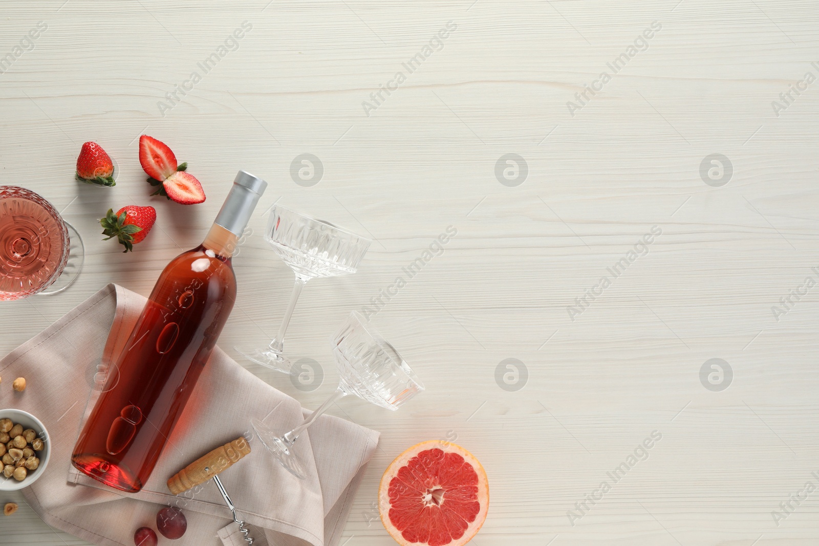 Photo of Flat lay composition with tasty rose wine, strawberries and grapefruit on light wooden table. Space for text