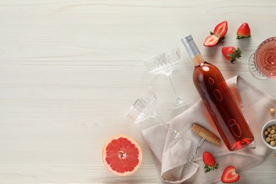 Flat lay composition with tasty rose wine, strawberries and grapefruit on light wooden table. Space for text