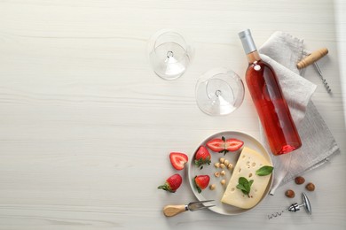 Flat lay composition with tasty rose wine and different food on light wooden table. Space for text