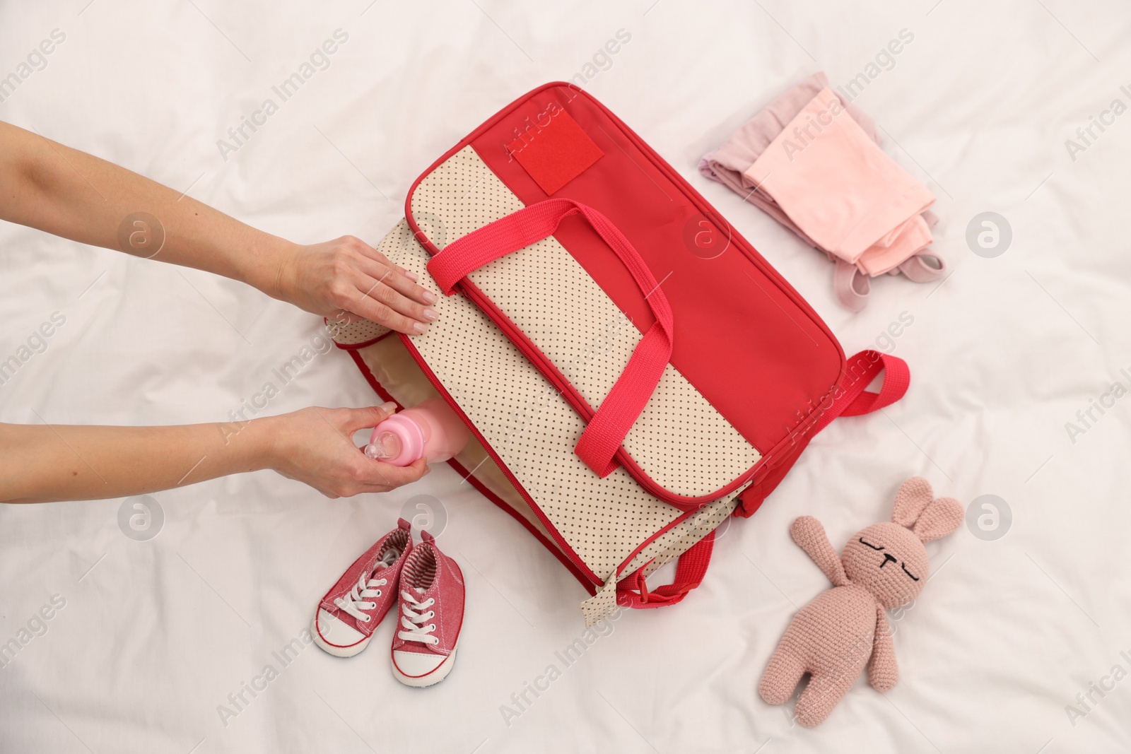 Photo of Mother packing baby's stuff into bag on bed, above view