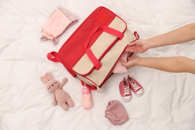 Photo of Mother packing baby's stuff into bag on bed, above view