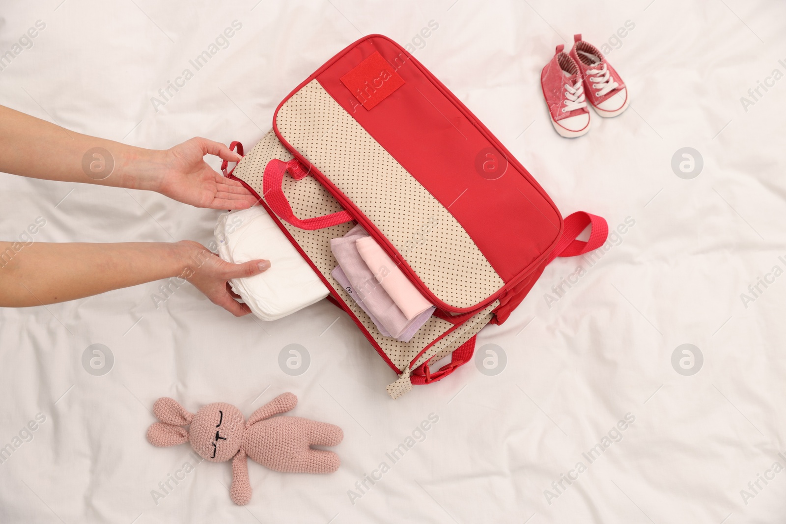 Photo of Mother packing baby's stuff into bag on bed, above view