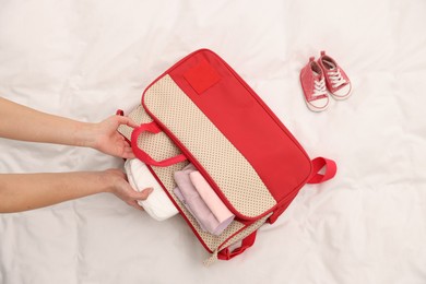 Photo of Mother packing baby's stuff into bag on bed, above view