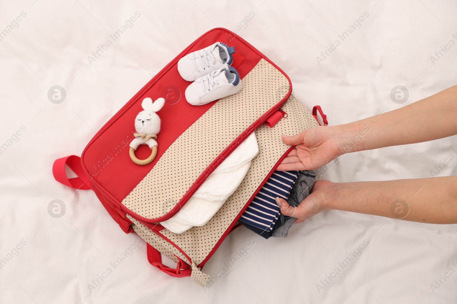 Photo of Mother packing baby's stuff into bag on bed, above view