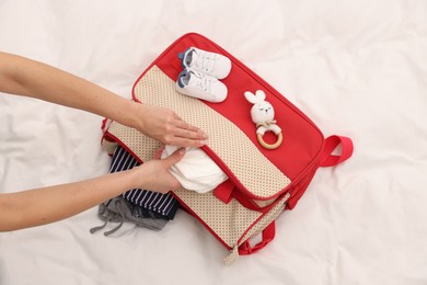 Photo of Mother packing baby's stuff into bag on bed, above view