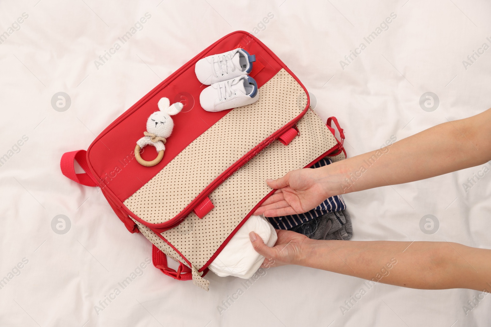 Photo of Mother packing baby's stuff into bag on bed, above view