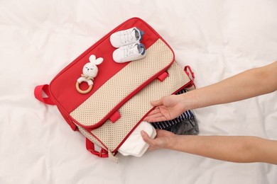 Photo of Mother packing baby's stuff into bag on bed, above view