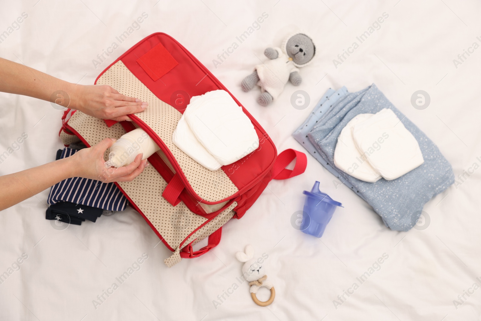 Photo of Mother packing baby's stuff into bag on bed, above view