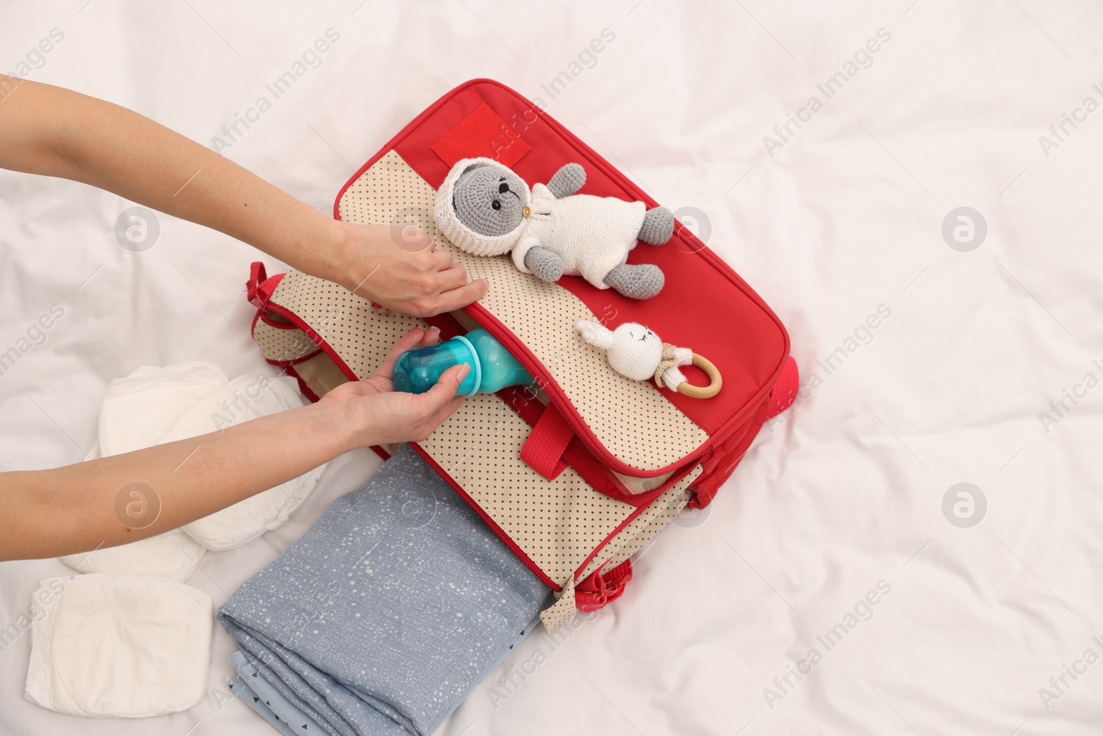 Photo of Mother packing baby's stuff into bag on bed, above view