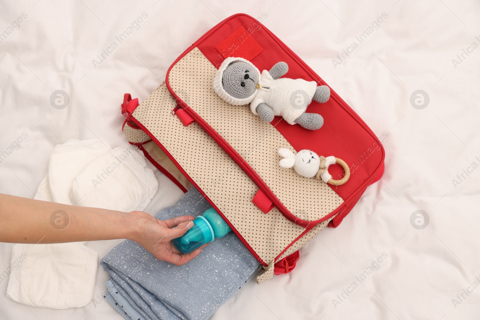 Photo of Mother packing baby's stuff into bag on bed, above view