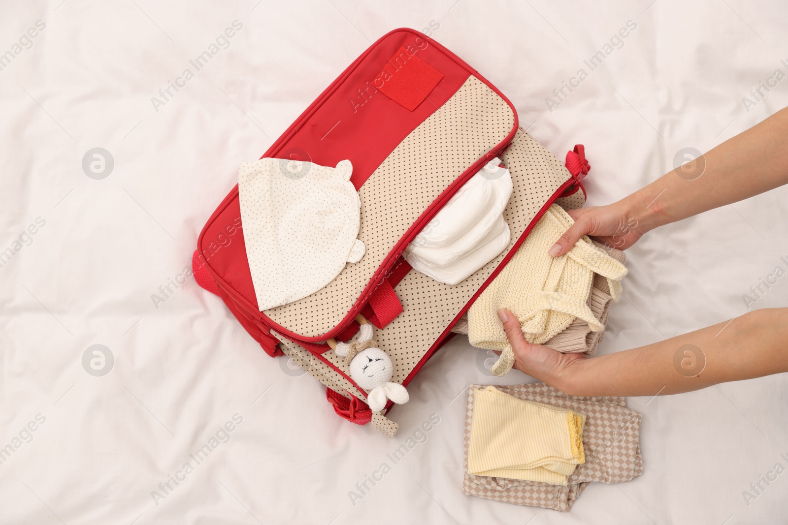 Photo of Mother packing baby's stuff into bag on bed, above view