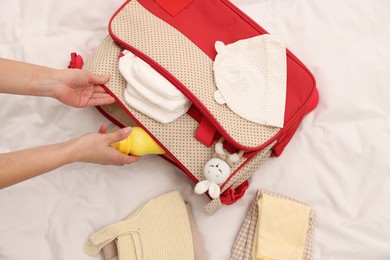 Photo of Mother packing baby's stuff into bag on bed, above view