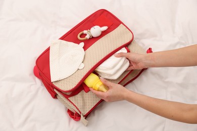 Photo of Mother packing baby's stuff into bag on bed, above view